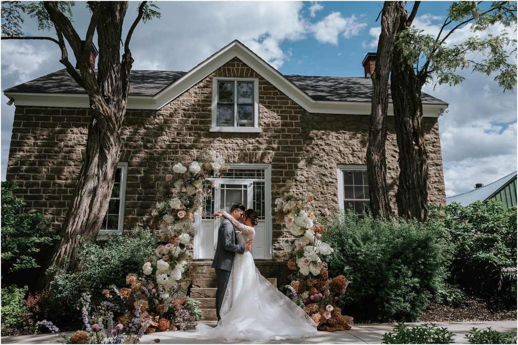 A romantic portait of a bride and groom hugging in front of the stone house at Stonefields Estate