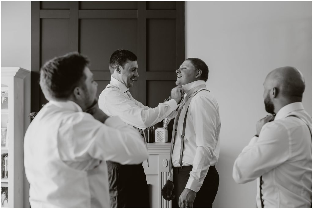 Groomsmen helping each other tie ties before the wedding ceremony. Photo by Cindy Lottes Photography