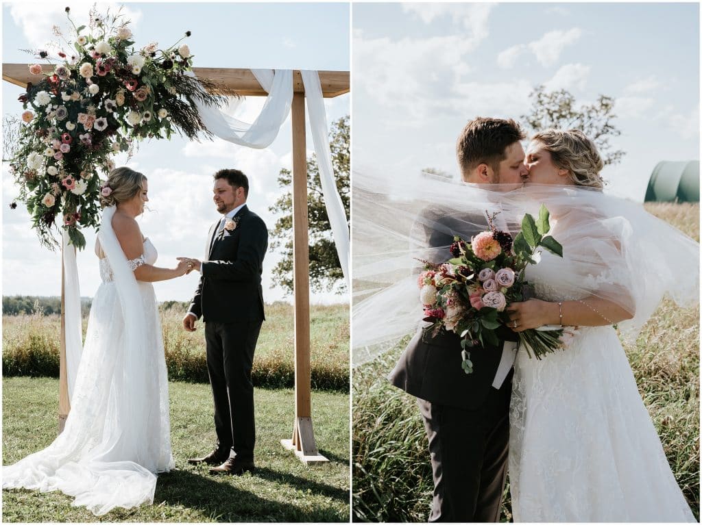 A couple exchange rings and take their first kiss under a wooden arch at their outdoor farm wedding in the Ottawa Valley. Photo by Cindy Lottes Photography