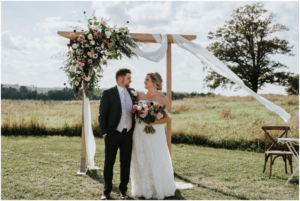 A bride and groom look into each other's eyes while standing in a field during their farm ceremony. Photo by Cindy Lottes Photography