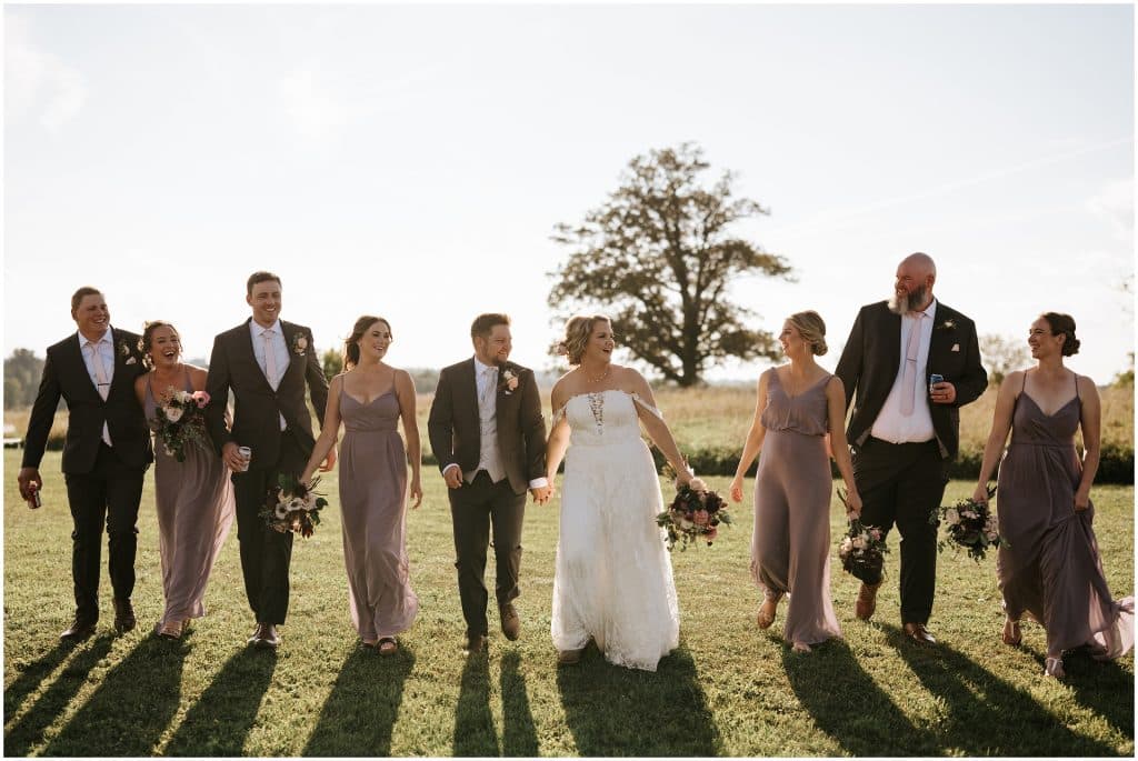 A wedding party walk and laugh in a field on a bright September day. Photo by Cindy Lottes Photography