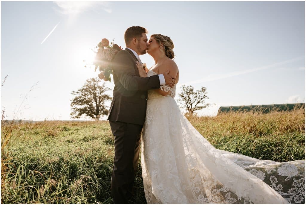 A bride and groom kiss in a field on their wedding day. Photo by Cindy Lottes Photography