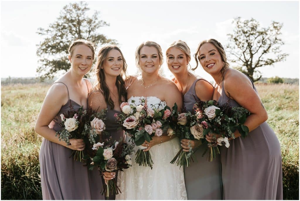 A bride and her bridesmaids pose for a portrait with their beautiful bouquets from Amethyst Floral. Photo by Cindy Lottes Photography