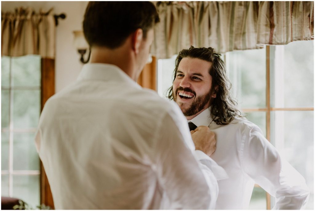 Best Man helps his brother the groom to do up his tie on the wedding day. Photo by Cindy Lottes Photography